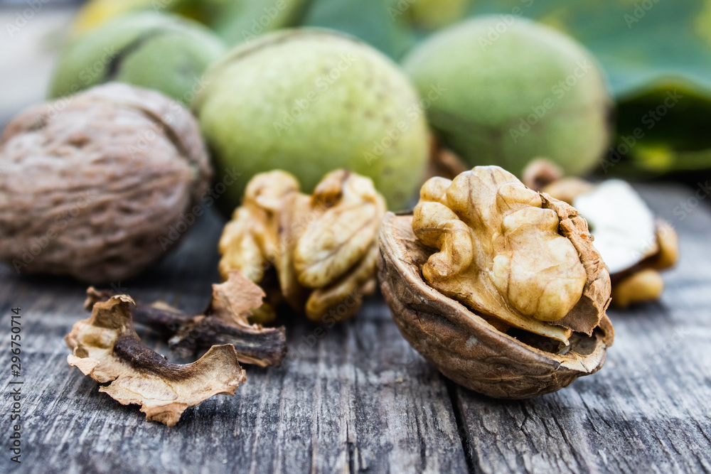 Walnut kernels and whole walnuts lie next to nuts in green shells and green leaves on a rustic old wooden table.