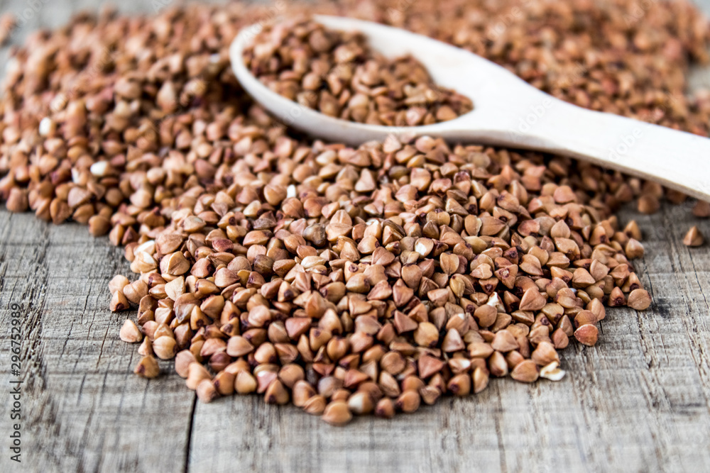 Uncooked buckwheat in a spoon on old boards. Buckwheat is used for cooking. Uncooked buckwheat in a spoon on old boards. Buckwheat is used for cooking.