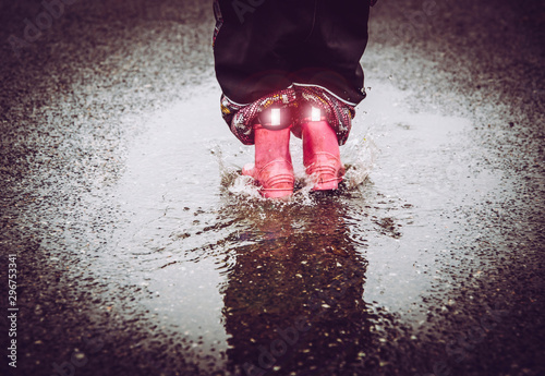 Girl having fun, jumping in water puddle on wet street, wearing rain boots with reflective detail fabric stripes shining. High visibility and safety in dark concept. photo