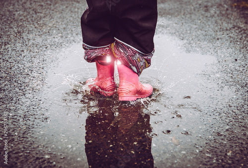 Girl having fun, jumping in water puddle on wet street, wearing rain boots with reflective detail fabric stripes shining. High visibility and safety in dark concept. photo
