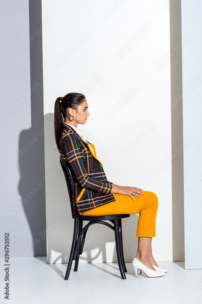 side view of attractive young woman sitting on chair on grey and white