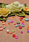 Yellow Crocheted flowers , green leaves and multicolored buttons on wooden  background.