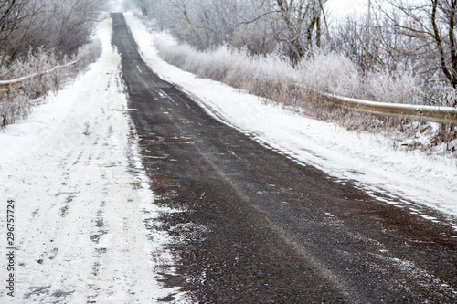 Rural asphalt road with trees covered up in hoar frost.