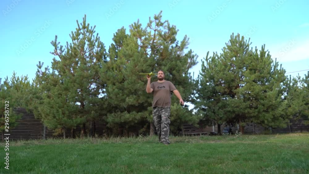 A bearded man launches a toy airplane on a background of pines and blue sky. A man plays with a toy airplane on a background of nature. A bearded man launches a toy airplane on a background of pines and blue sky. A man plays with a toy airplane on a background of nature.