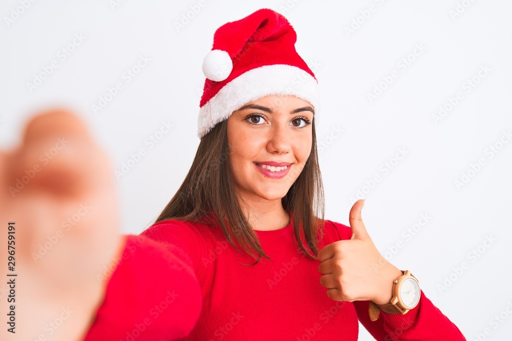 Girl wearing Christmas Santa hat make selfie by camera over isolated white background happy with big smile doing ok sign, thumb up with fingers, excellent sign Girl wearing Christmas Santa hat make selfie by camera over isolated white background happy with big smile doing ok sign, thumb up with fingers, excellent sign