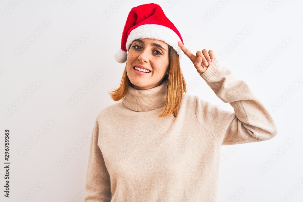 Beautiful redhead woman wearing christmas hat over isolated background Smiling pointing to head with one finger, great idea or thought, good memory Beautiful redhead woman wearing christmas hat over isolated background Smiling pointing to head with one finger, great idea or thought, good memory