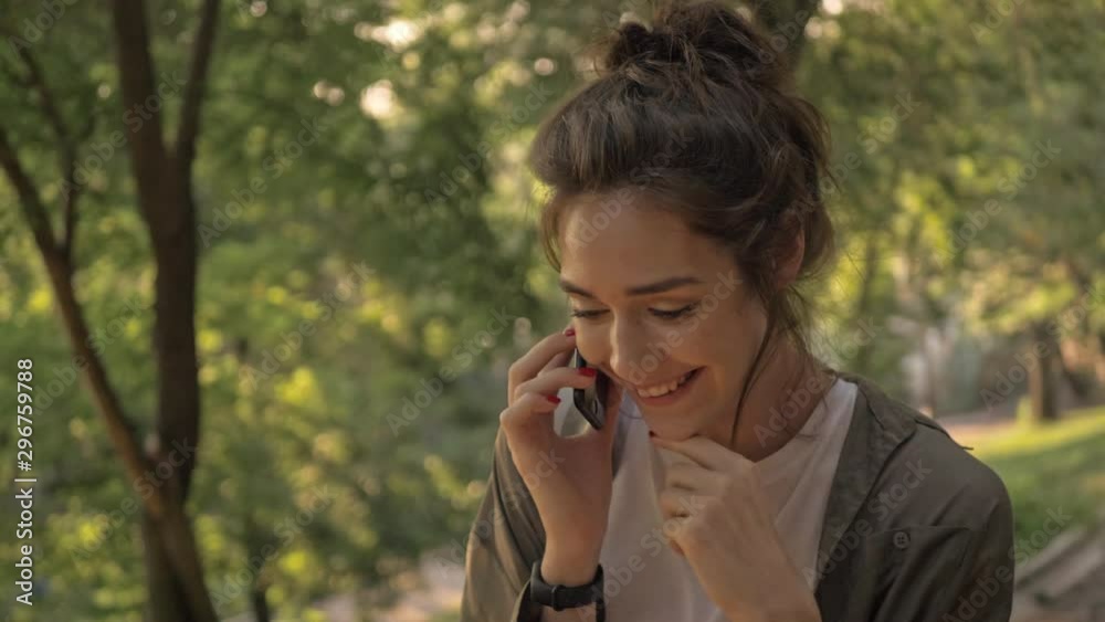 Attractive young brunette woman smiling and talking on smartphone while walking in the park Attractive young brunette woman smiling and talking on smartphone while walking in the park