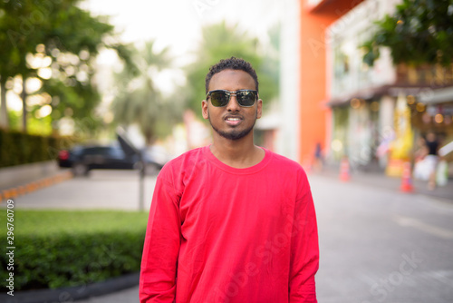 Happy young African bearded man with sunglasses smiling at the city streets