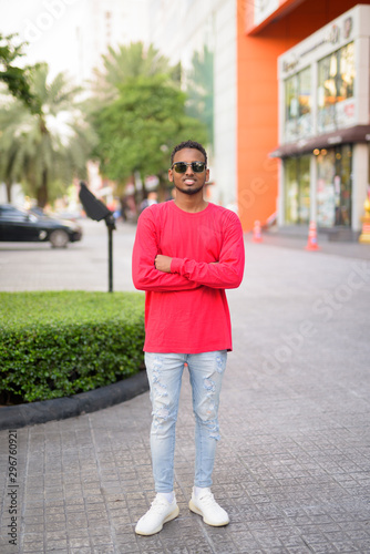 Full body shot of happy young African man smiling with sunglasses in the city