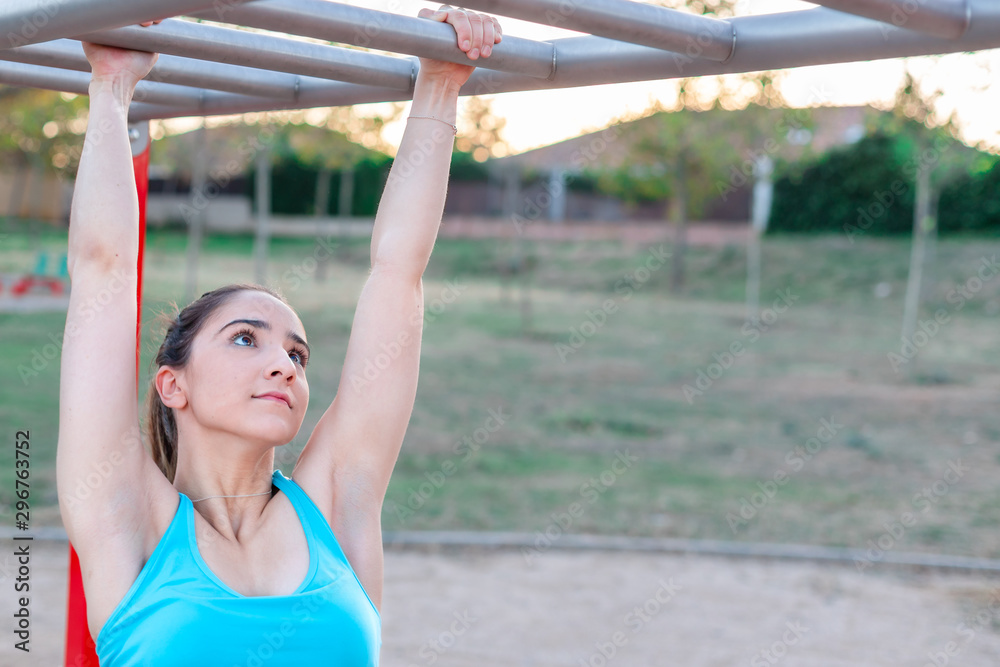 Fototapeta premium Young caucasian woman hanging with arms outstretched in a park's training area.