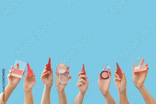 Many hands with decorative cosmetics on color background