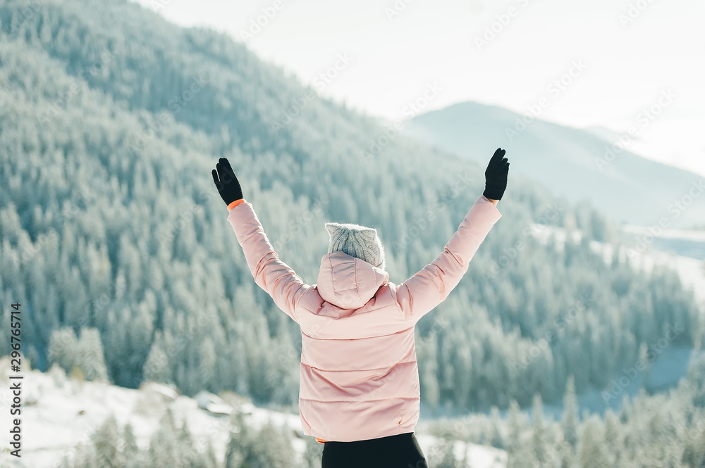 Happy woman in jacket standing and raising hands up in snowy mountain scenery. Bac view.