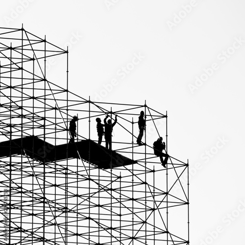 Fototapeta Five construction workers building a metallic scaffold