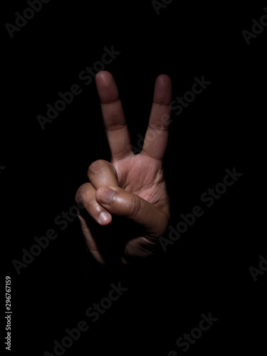 Low key photo of a man showing two fingers indicating the number two or the victory sign