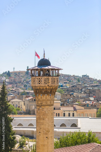 Ancient mosque minaret with loudspeakers calling for prayer and a Turkish flag in the city of Gaziantep, Turkey. In the background houses on a hill. Panoramic city view photo