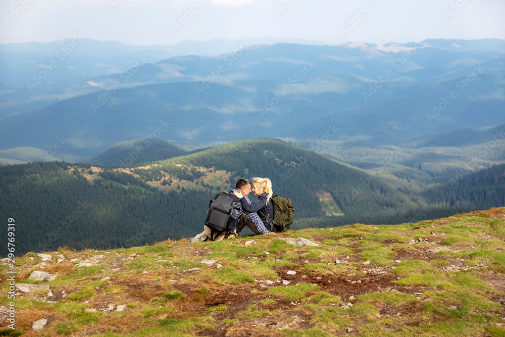 Couple sitting on top of a mountain. Beautiful landscape of mountains and forests against the blue sky. Travel concept.