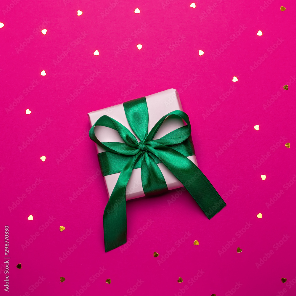 Wrapped present or giftbox with green ribbon on deep red or magenta background with hearts confetti, copy space, top view, flat lay. Background for Valentine's Day, Mother's Day or anniversary Wrapped present or giftbox with green ribbon on deep red or magenta background with hearts confetti, copy space, top view, flat lay. Background for Valentine's Day, Mother's Day or anniversary