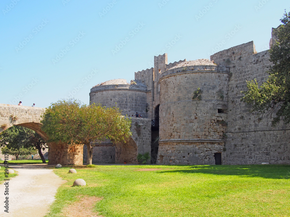 people crossing the amboise gate in the medieval walls of the old city in rhodes town surrounded by grass and trees