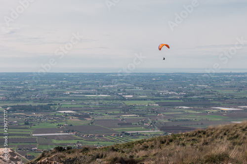 Paraglider flying over valley in Italy, cloudy sky