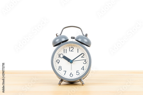 Grey alarm clock on wooden desk on white background