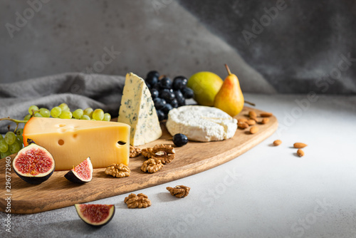 Cheese plate served with camembert, brie, blue cheese, maasdam, grapes, pear, figs and nuts on a wooden board on gray background. Side view. Copy space. Dairy products, keto diet photo