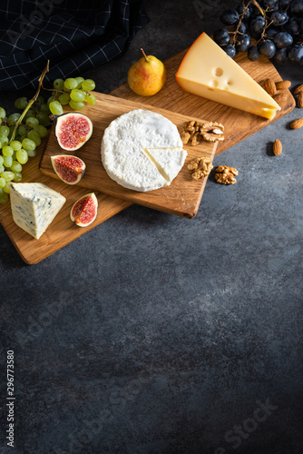 Cheese plate: Maasdam, Camembert cheese, blue cheese, figs, walnuts, almonds, pears and grapes on wooden board on gray background. Copy space for text. Top view, falt lay. Appetizer, menu photo