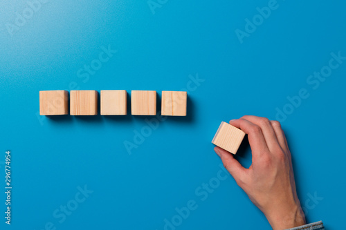 Woman's hand establishes a wooden cubes in row. Blank wooden blocks for word, text or illustration. Hand placing cube and finishing the row