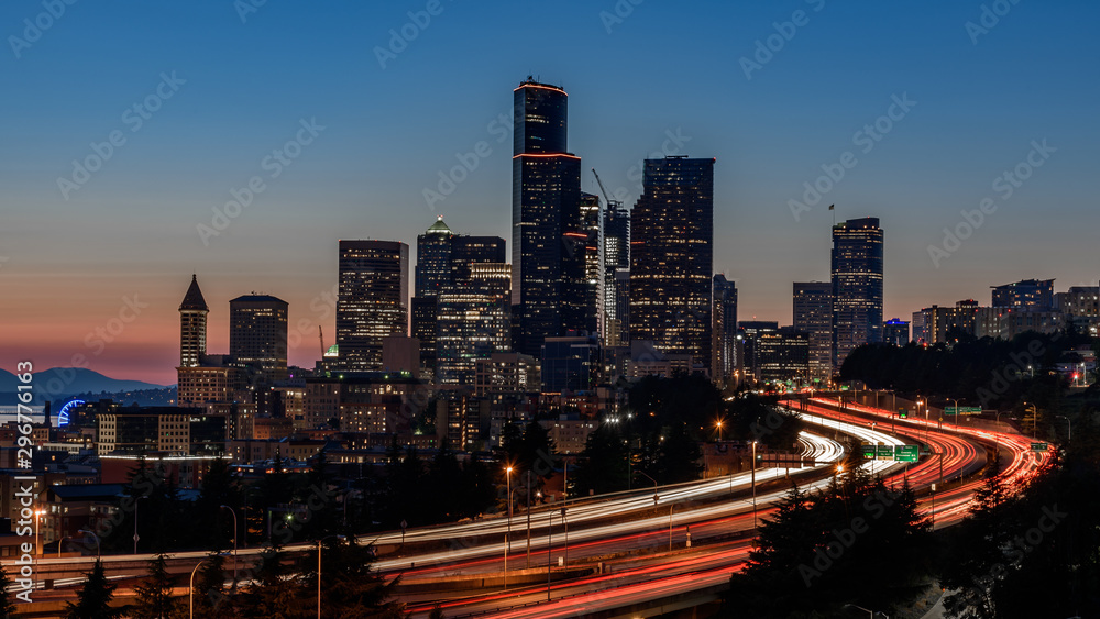 Fototapeta premium Seattle skyline, at sunset. The cars along the highway are creating light trails, due to a slow shutter speed