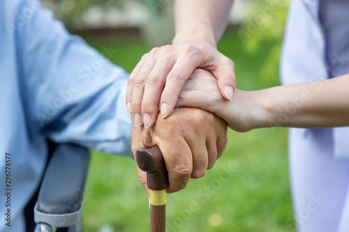 Nurse holding elderly man hand with cane on wheelchair in garden close up