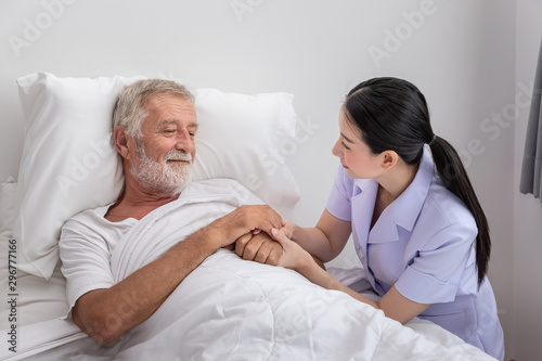Happy nurse holding elderly man hands with blanket in bedroom at nursing home