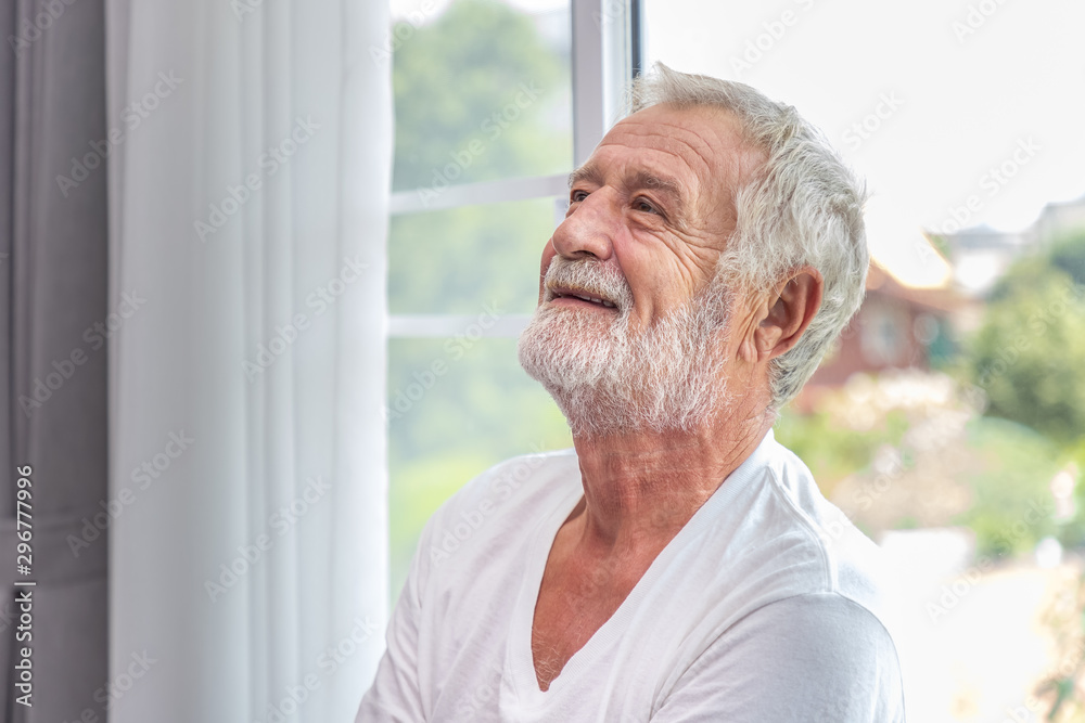 Senior elderly man standing at window in bedroom after waking up in morning Senior elderly man standing at window in bedroom after waking up in morning