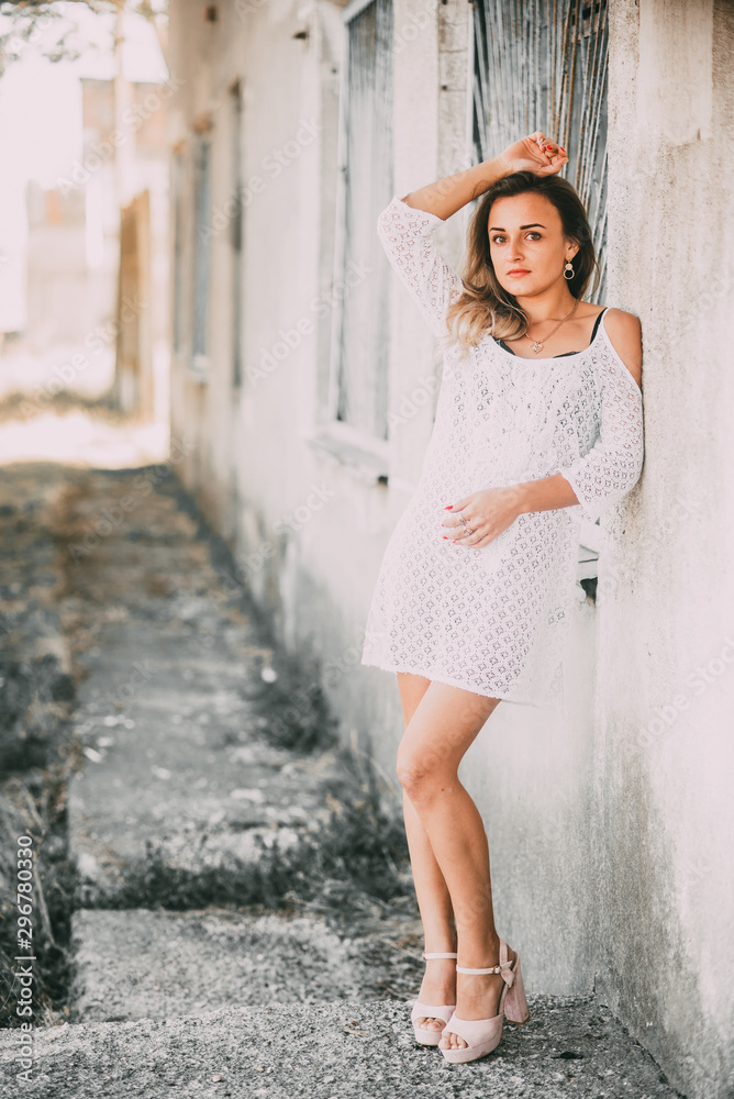 Beautiful and sexy girl in a white light dress on a bright Sunny day next to the old staircase