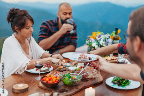 Friends and family gathered for picnic dinner for Thanksgiving. Festive young people celebrating life with red wine  grapes  cheese platter  and a selection of cold meats