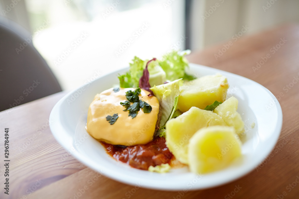 Boiled potatoes with green salad, vegetables and cutlet. Plate with homemade food on a wooden dinner table. Cooked potato dish