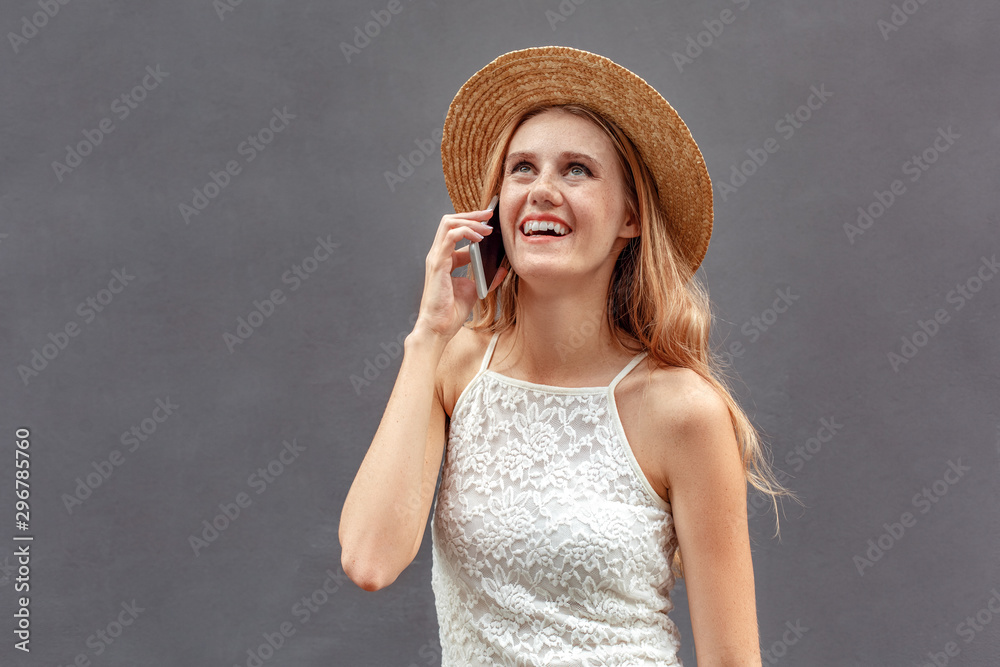 Freestyle. Young woman in hat standing isolated on wall talking on smartphone laughing cheerful