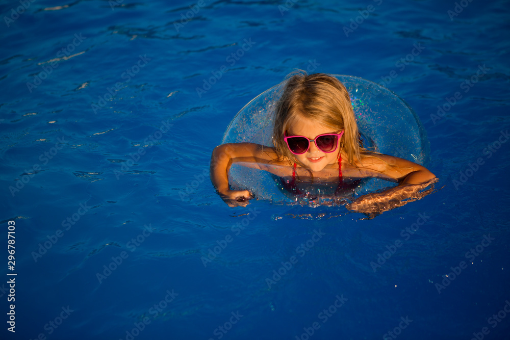 little blonde girl in sunglasses swims in pool with swimming circle