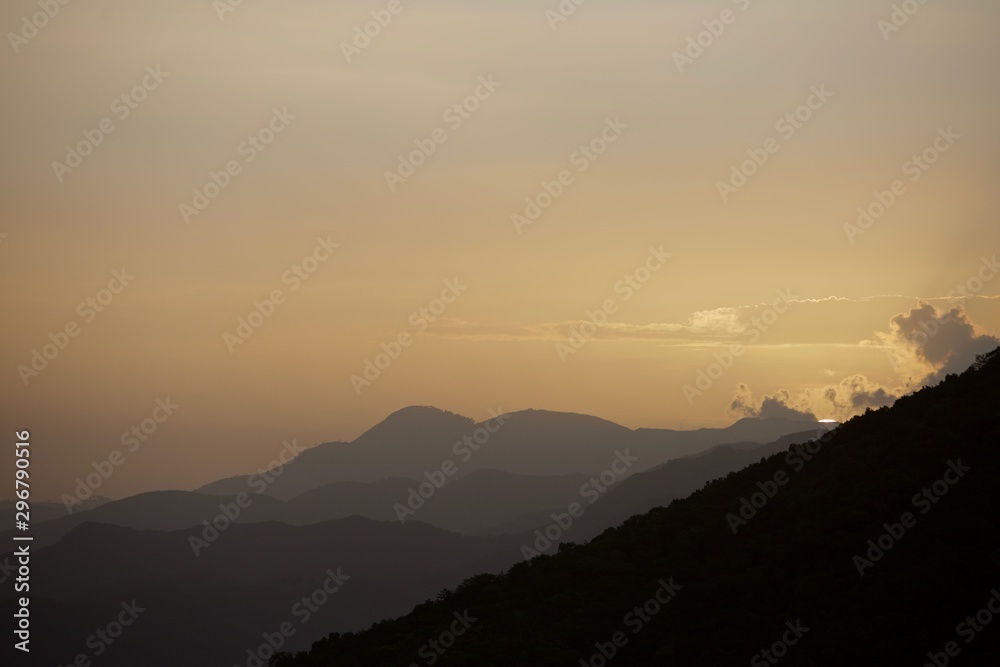 dramatic beautiful sunset with layered mountains in forground and sliver of sun seting