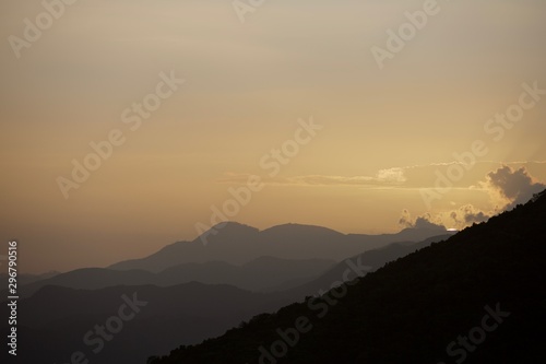 dramatic beautiful sunset with layered mountains in forground and sliver of sun seting