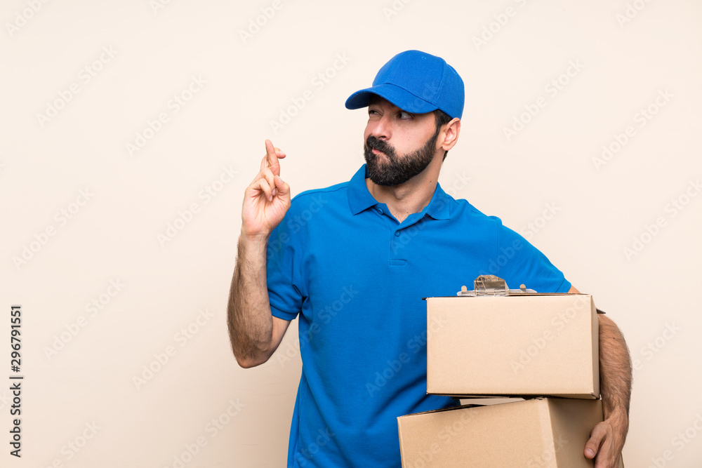 Delivery man with beard over isolated background with fingers crossing and wishing the best Delivery man with beard over isolated background with fingers crossing and wishing the best