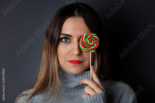 beautiful and young woman with colorful Christmas candy in hands on dark background
