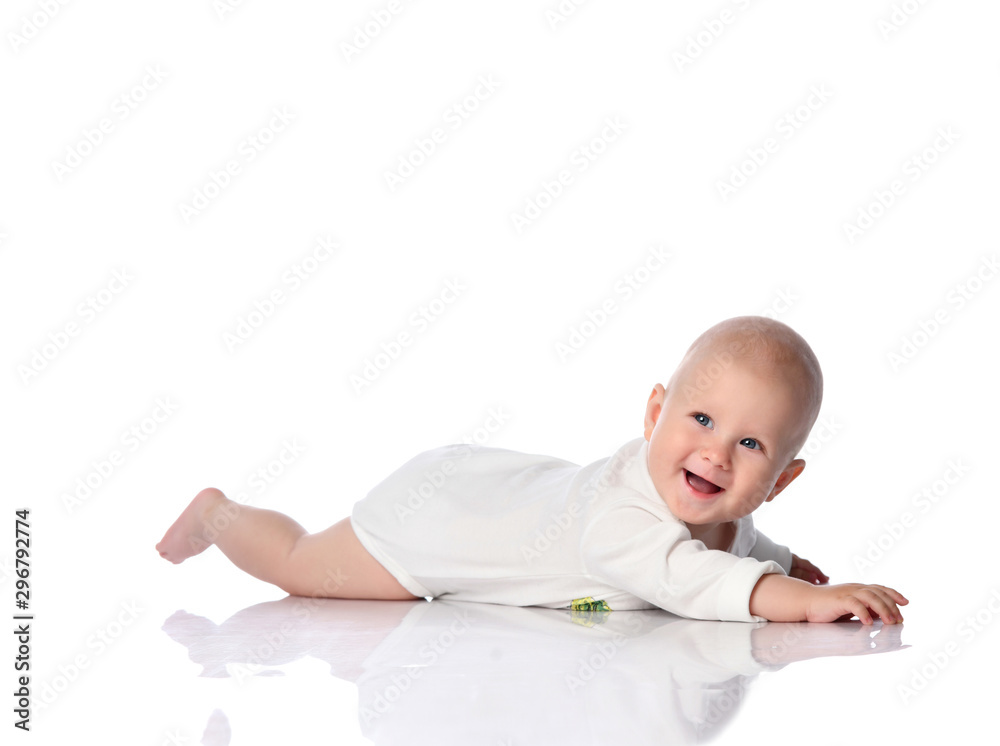 Smiling infant child baby toddler in white bodysuit lying on his stomach crawling, trying to reach something on white Smiling infant child baby toddler in white bodysuit lying on his stomach crawling, trying to reach something on white