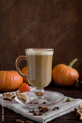 One Pumpkin spice latte in a tall glass on a wooden background. Autumn mood. Cinnamon, pumpkin, cloves, spices and cookies. Side view, close-up, copy space.