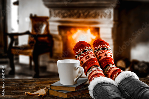 Legs in winter christmas socks on wooden top board with fireplace background in cozy home interior.