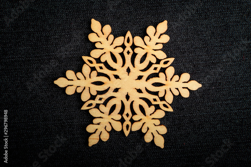 One delicate light brown wooden snowflake on black textile material background, displayed on centre, top view with space for text around, flat lay with laser cut wooden object © Cristina Ionescu