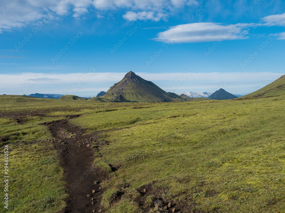 Volcanic landscape with footpath of Laugavegur trek and green Storasula mountain with lush moss and low clouds. Fjallabak Nature Reserve, Iceland. Blue sky background, copy space.