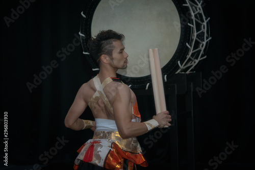 Taiko drummer hits the big drum on stage on a black background, back view. photo