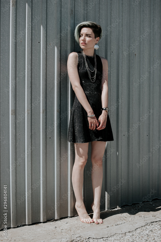 Beautiful girl in little black dress with short blue fashionable hairstyle standing barefoot on the ground near metal textured wall. Full-length photo Stock Photo | Adobe Stock Beautiful girl in little black dress with short blue fashionable hairstyle standing barefoot on the ground near metal textured wall. Full-length photo Stock Photo | Adobe Stock