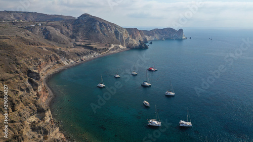 Aerial drone photo of iconic famous White beach with deep rocky and volcanic turquoise sea visited by sail boats, Santorini island, Cyclades, Greece