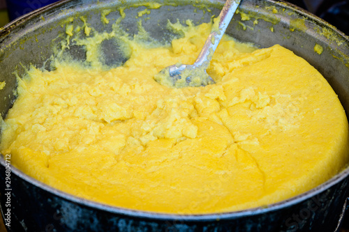 Polenta being traditionally prepared in a large pan, cooked at a street food market, selective focus