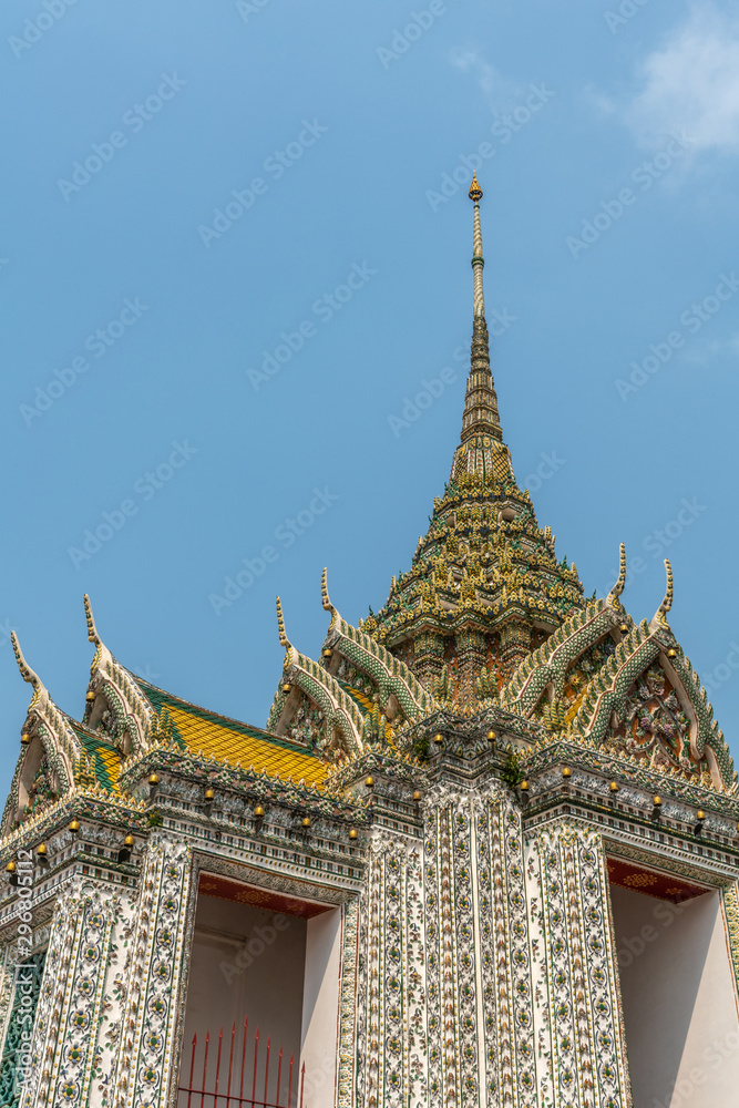 Bangkok city, Thailand - March 17, 2019: Gables and greenish spire of smaller section of Temple of Dawn, with its colorful porcelain faience surface, golden roof, against blue sky.